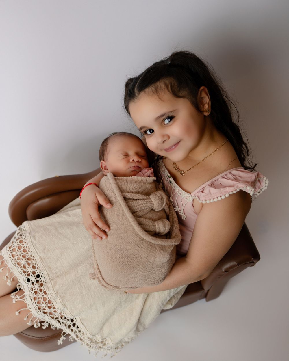 Two people in pink and beige tones sitting together in a gentle embrace with lace details and soft lighting.