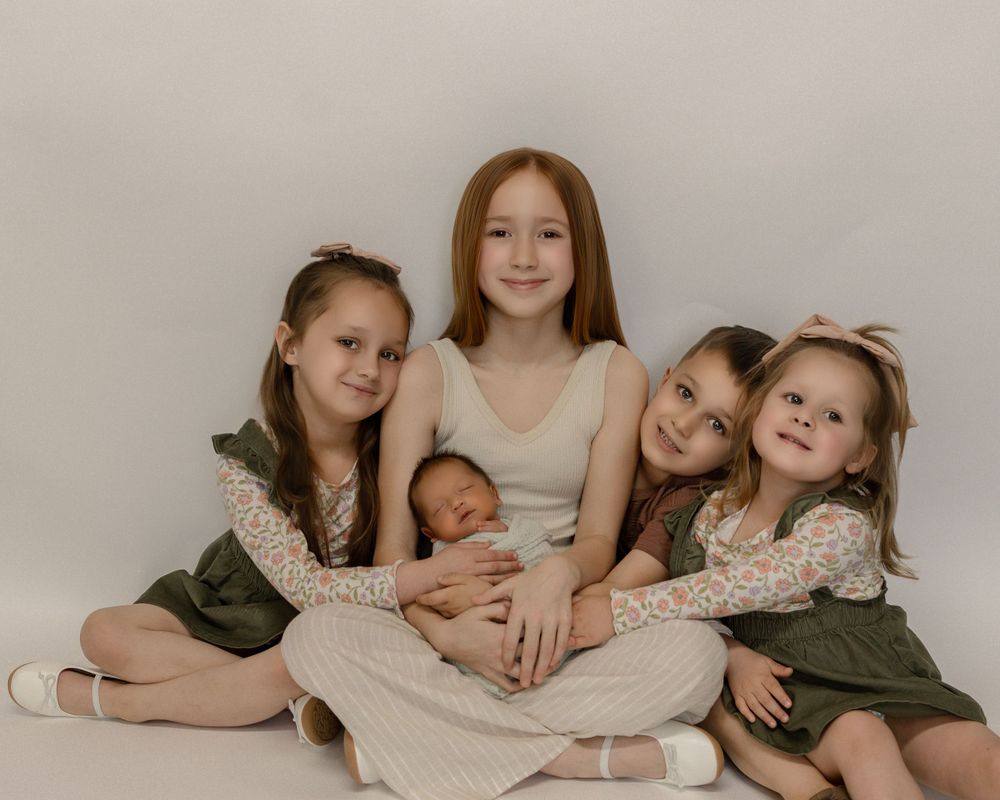 Five siblings in coordinated green and cream outfits pose together for a classic studio portrait against a neutral backdrop.