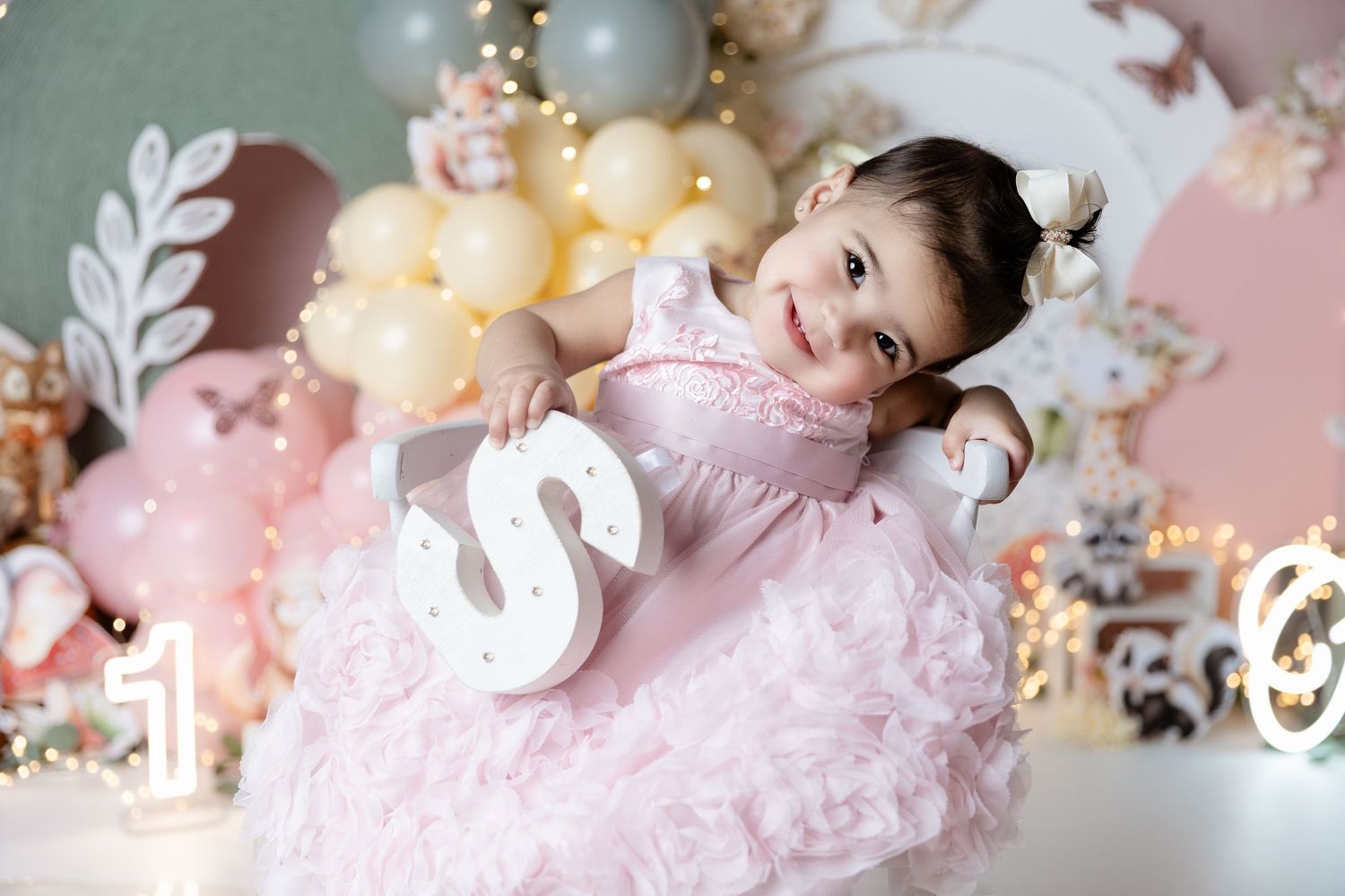 Pink tulle party dress and decorative swan prop amid pastel balloon decor and floral arrangements in soft studio setting.