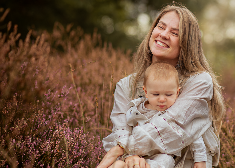 Moeder knuffelt haar baby lachend tussen de bloeiende heide.