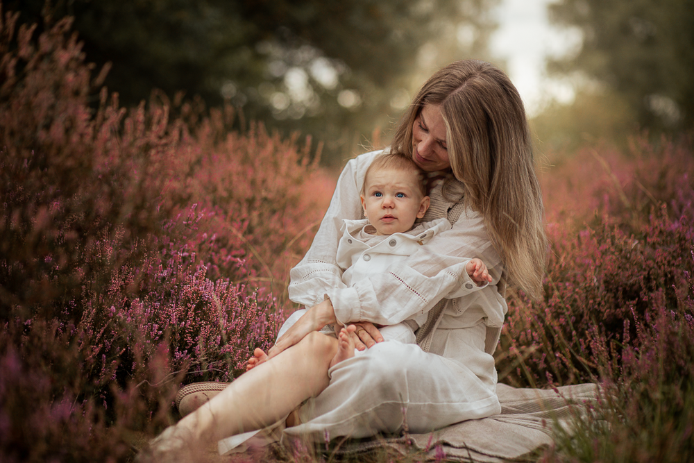 Moeder zit met haar baby in de heide, liefdevol moment in de natuur.