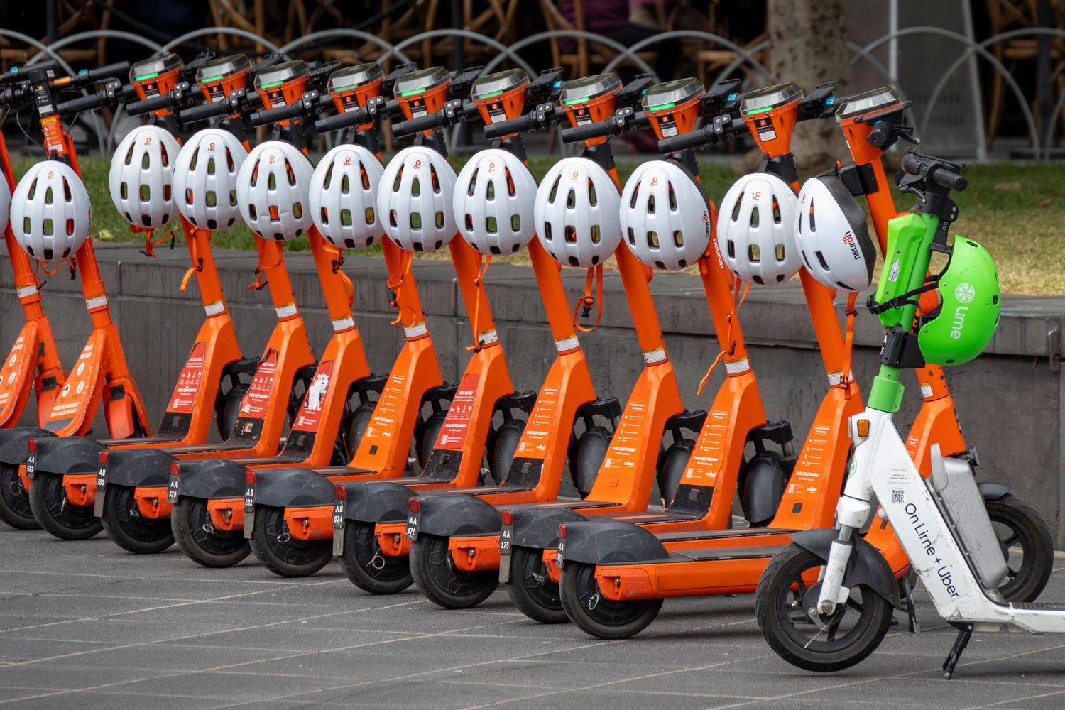 Row of bright orange electric scooters parked neatly in formation, each with a white helmet attached to the handlebar.