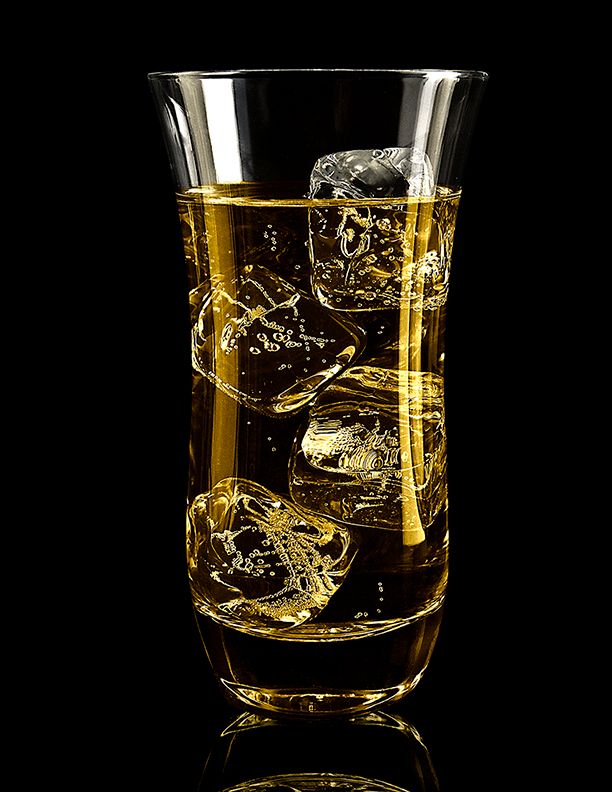 Glass of golden whiskey with ice cubes on black background showing liquid reflections and bubbles.
