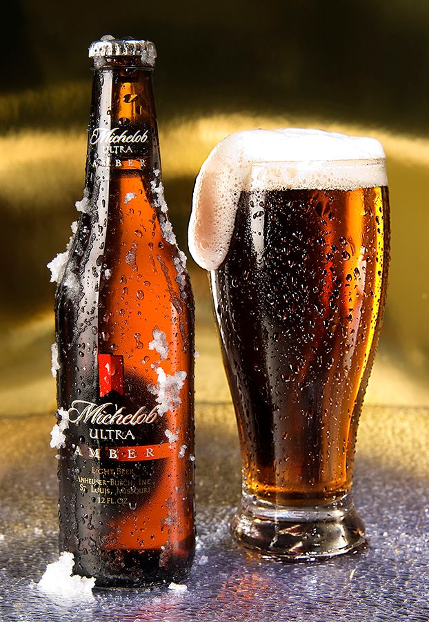A cold Michelob beer bottle with condensation and a full glass of amber beer with frothy head on reflective surface.