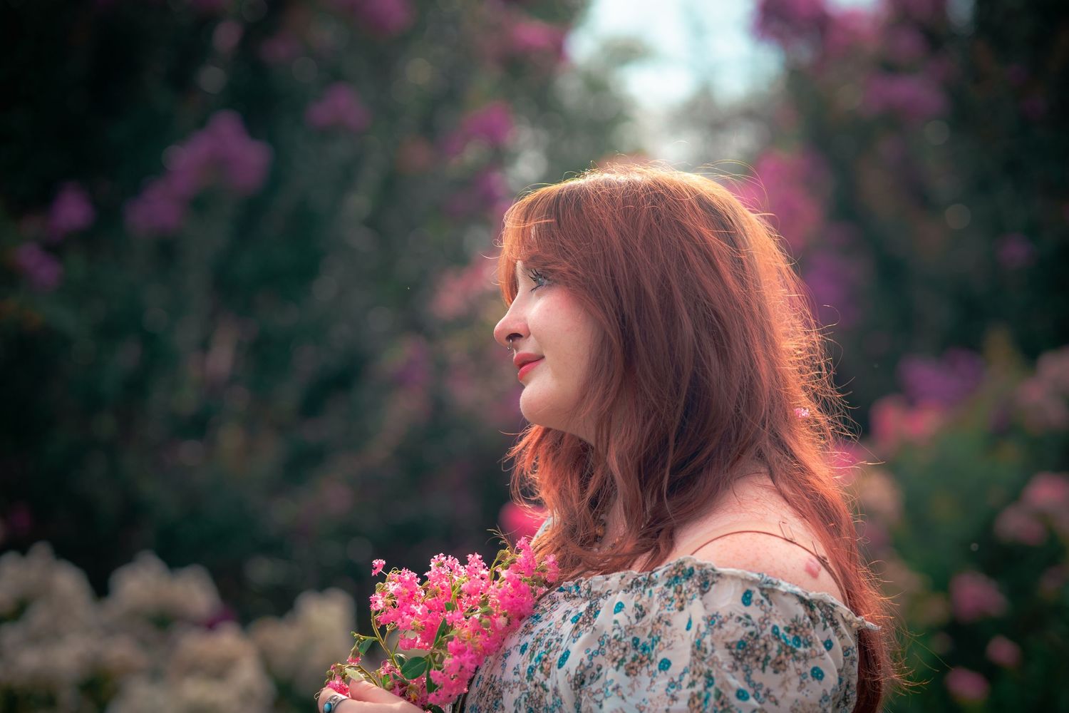 Side profile portrait of person with curly hair resting chin on hand against nature backdrop.