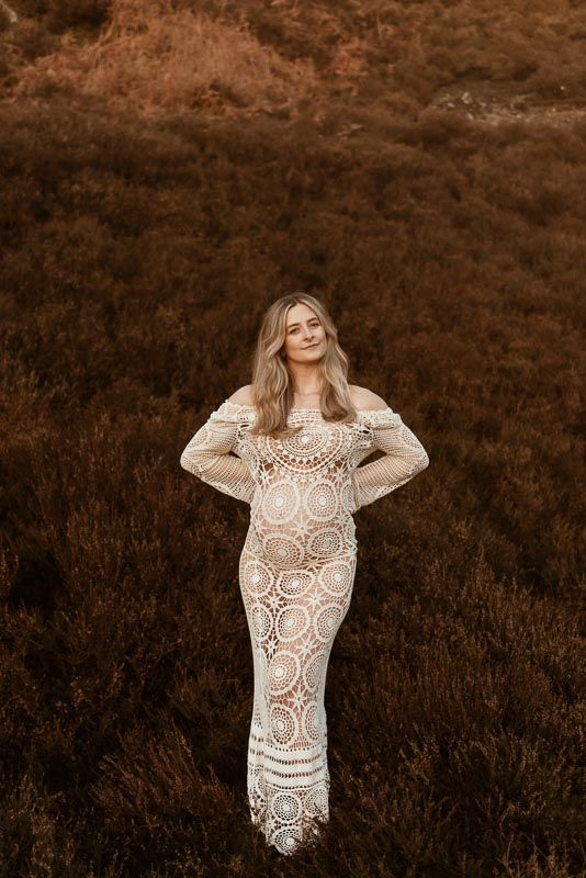 Ethereal lace wedding dress with intricate circle patterns photographed against rustic brown autumn field backdrop.