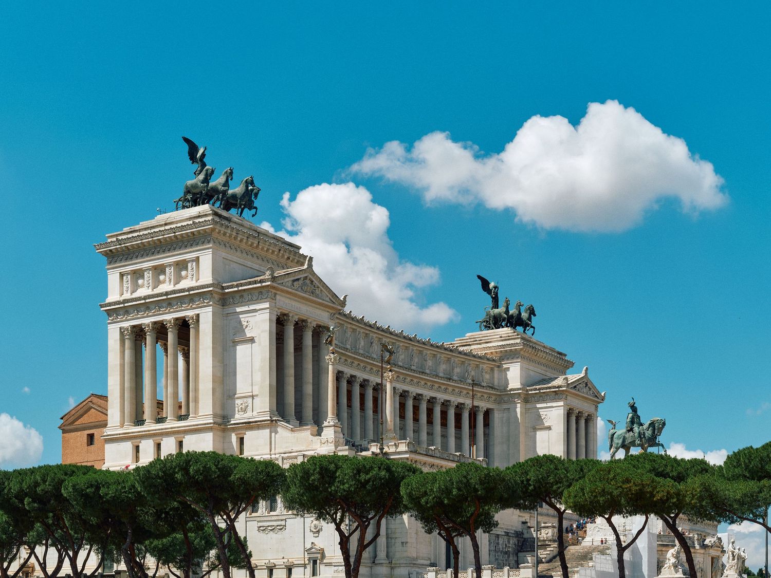 The Vittorio Emanuele II Monument in Rome features white marble columns and bronze equestrian statues against a blue sky.