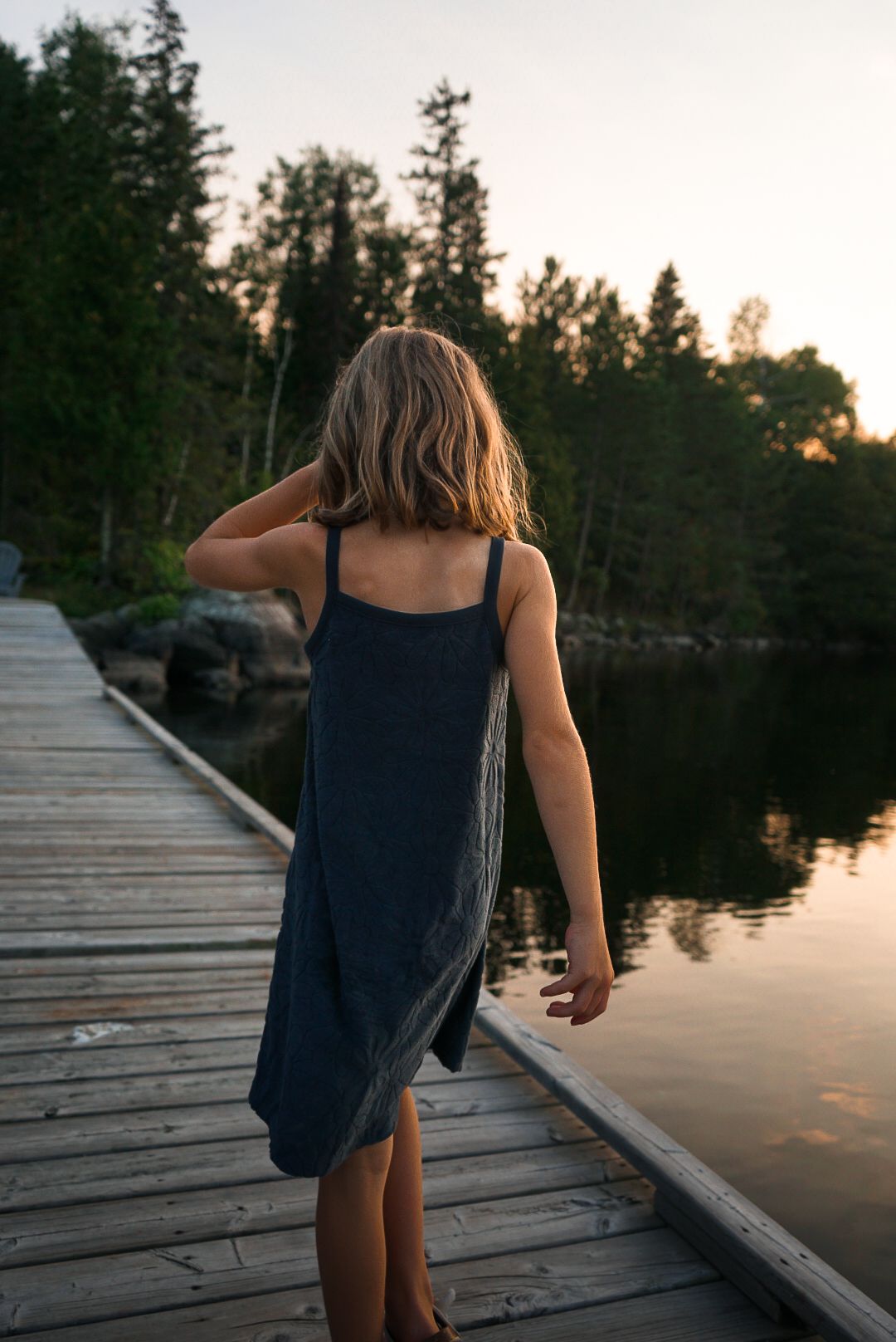 Person walking on a wooden dock by the lake at sunset.