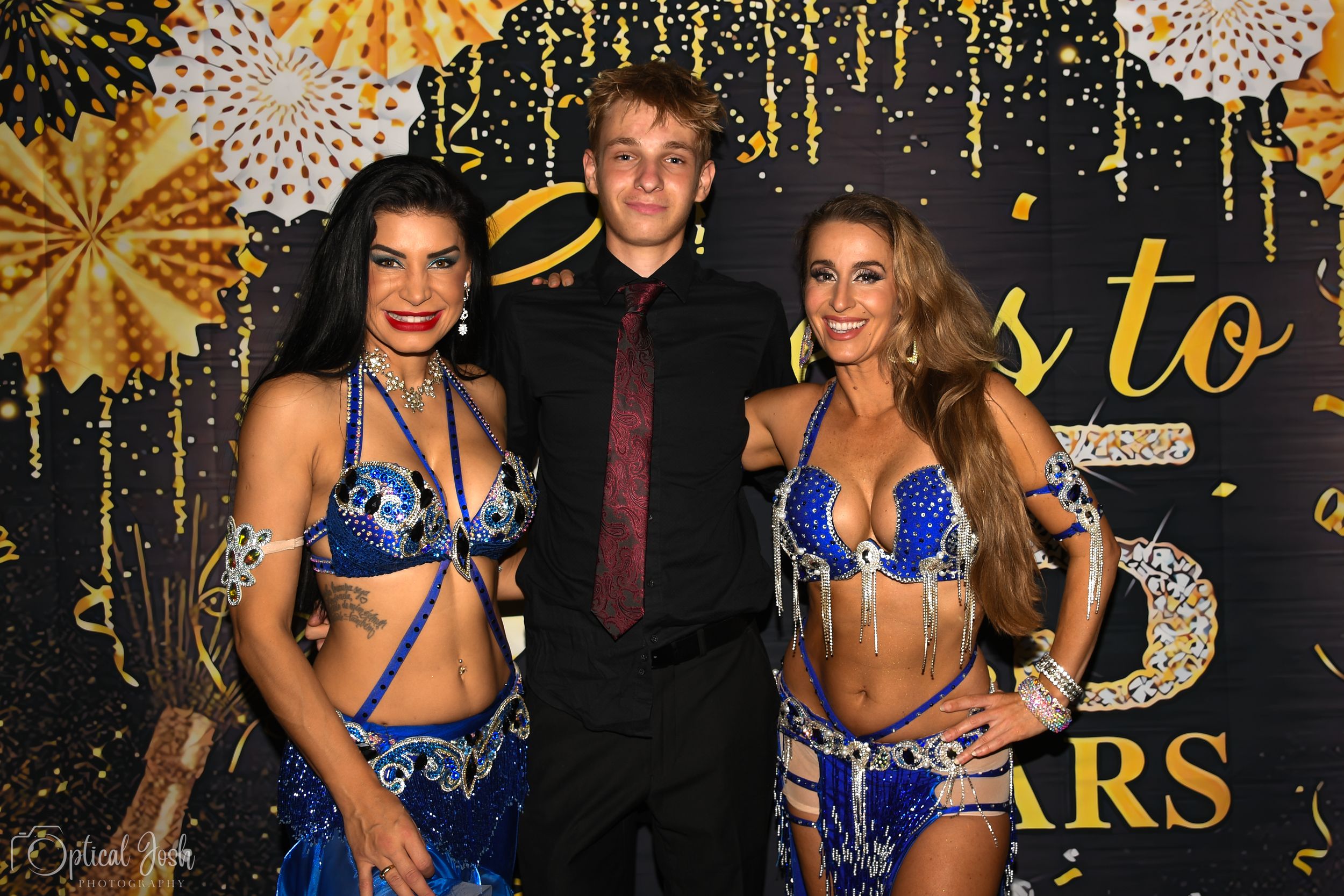 Three people pose at a formal event with gold decorative backdrop and firework patterns.