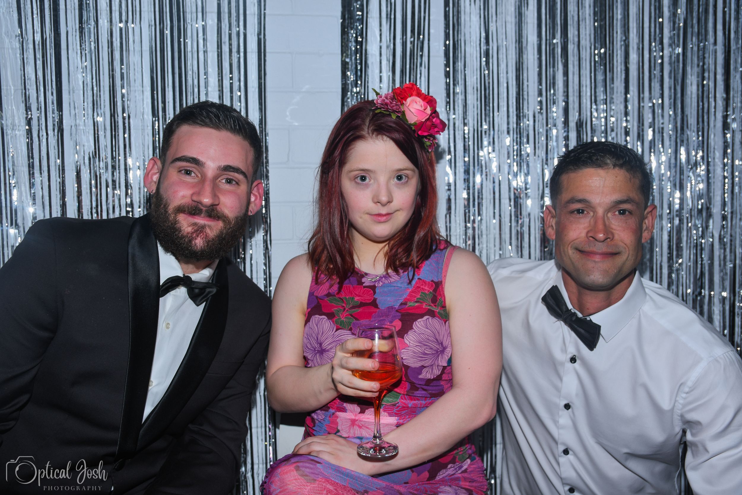 Three people pose together at a party against a silver tinsel backdrop.