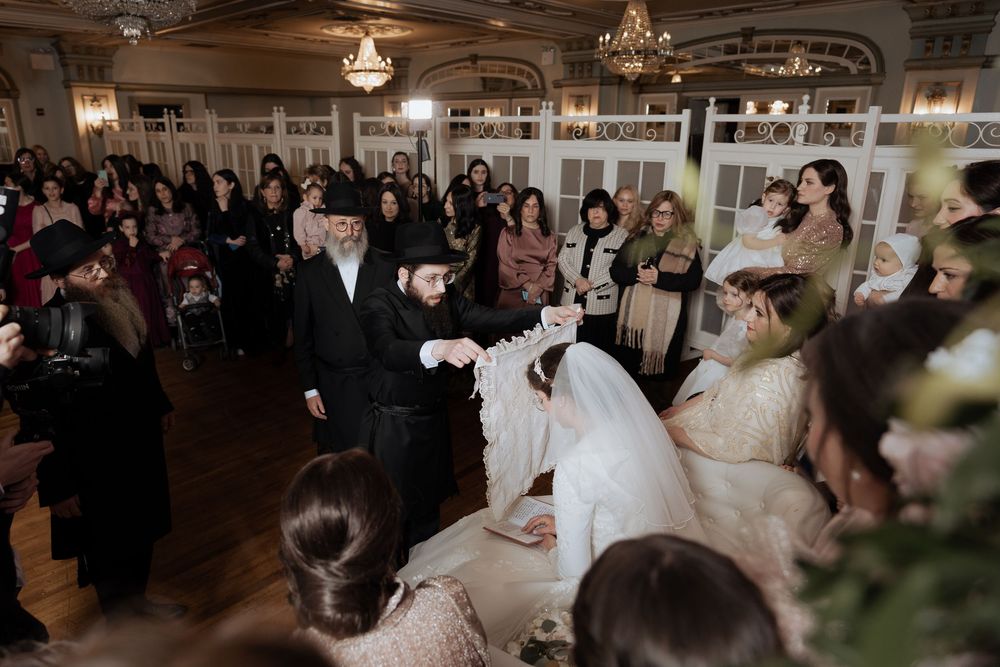 Large wedding crowd celebrating during a traditional Jewish ceremony in an ornate venue.