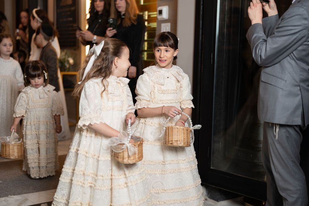 Young flower girls in vintage-style cream lace dresses carry woven baskets.