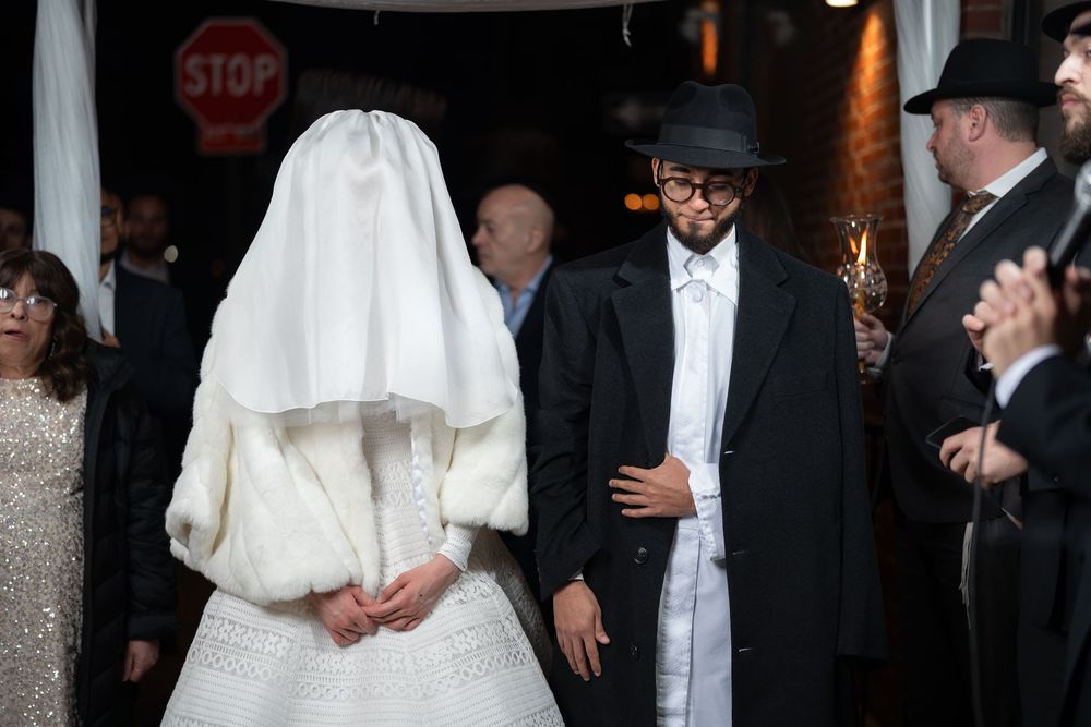 Wedding couple in traditional Orthodox Jewish attire stand outside venue.