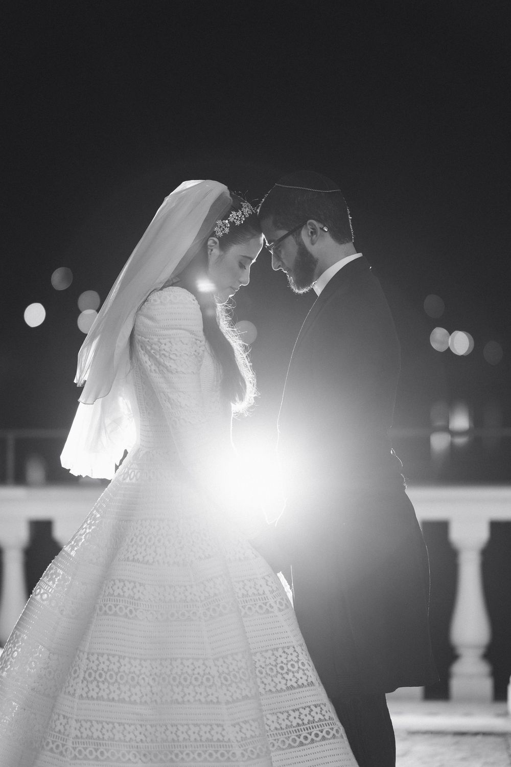 An intimate black and white portrait of a couple in wedding attire with dramatic backlighting.