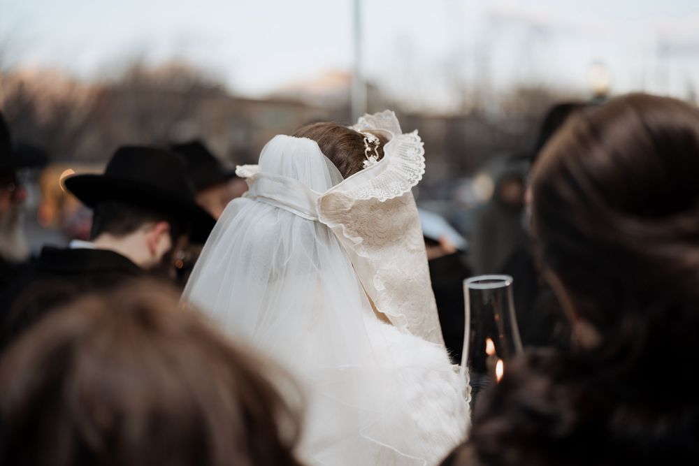 Close-up of bride's veil amid crowd at Orthodox Jewish wedding celebration.