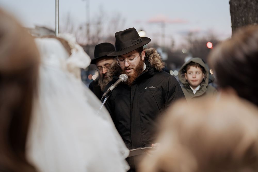A crowd gathered outdoors in winter with someone wearing a hat and coat in focus.
