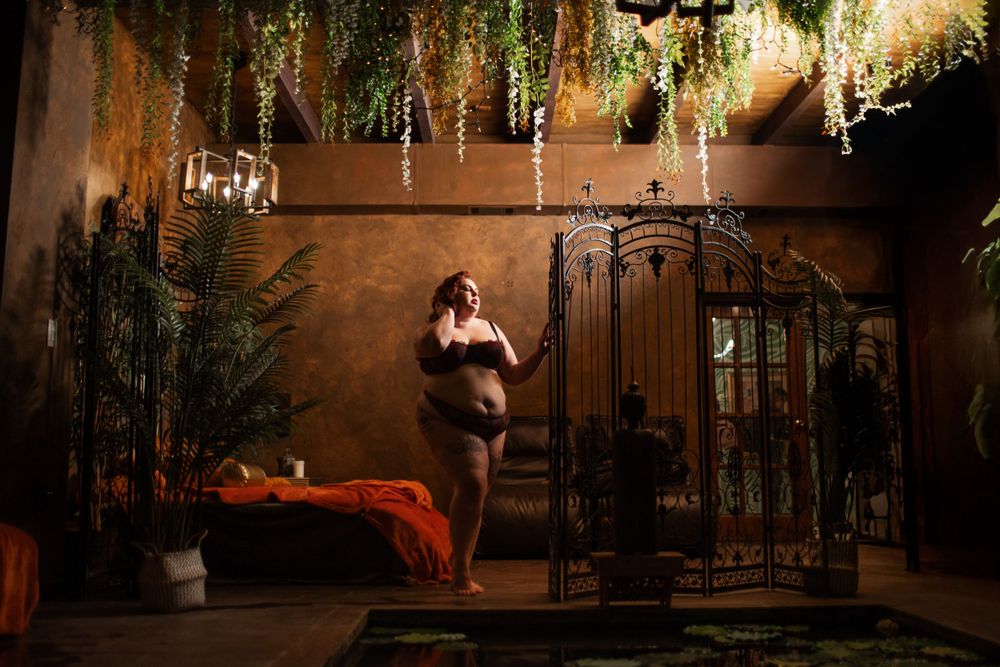 A romantic boudoir photography session in an intimate indoor setting with hanging wisteria and moody lighting.