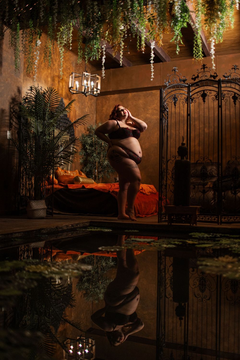 Artistic maternity photoshoot in dark room with hanging wisteria and reflective floor creating mirror effect.