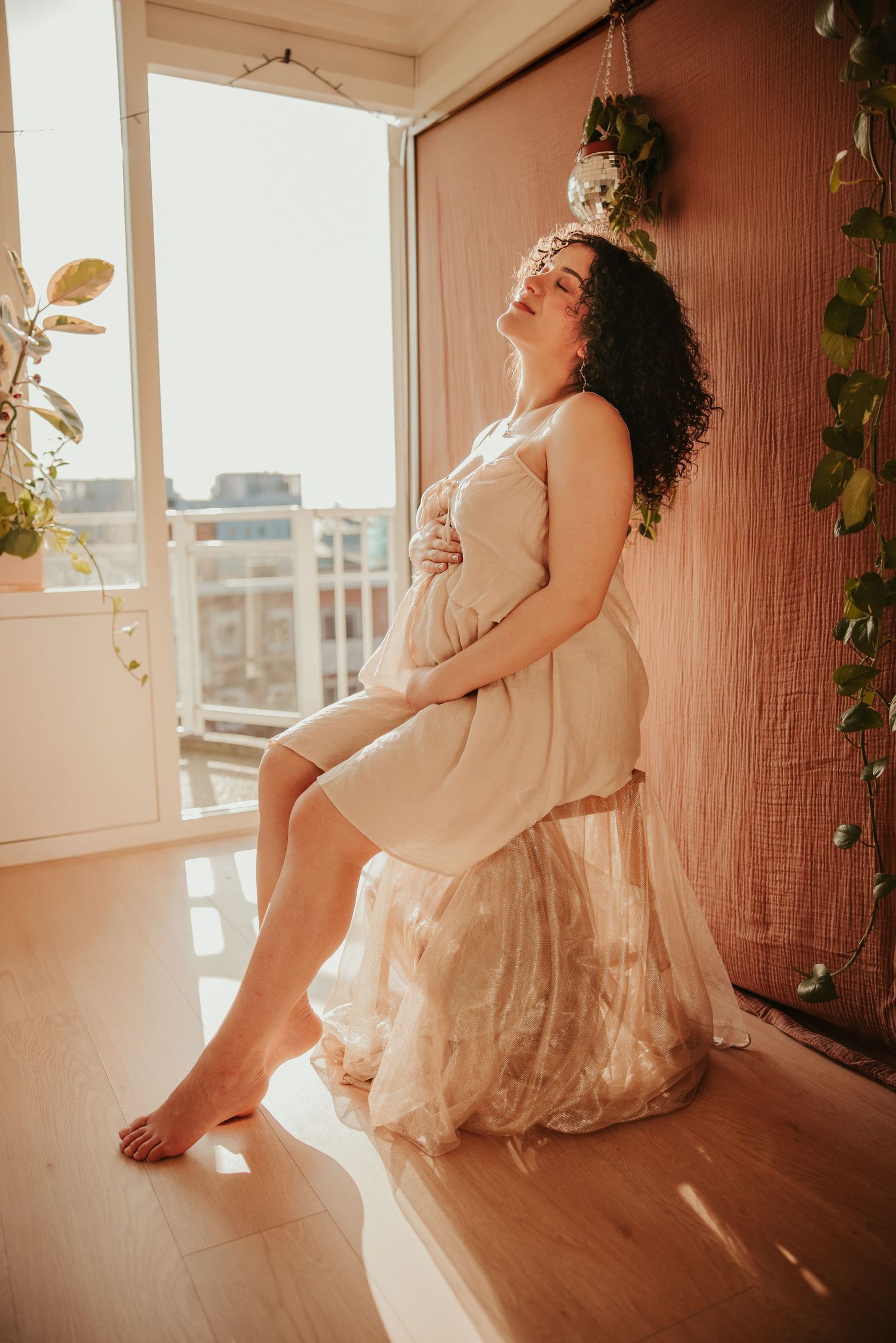 A dreamy pregnancy photoshoot in warm natural light features ethereal poses against a window and linen backdrop