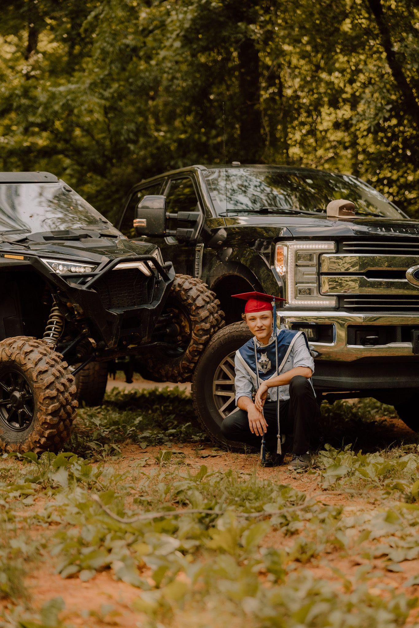 ATV and black pickup truck parked in autumn woods with fallen leaves on the ground.