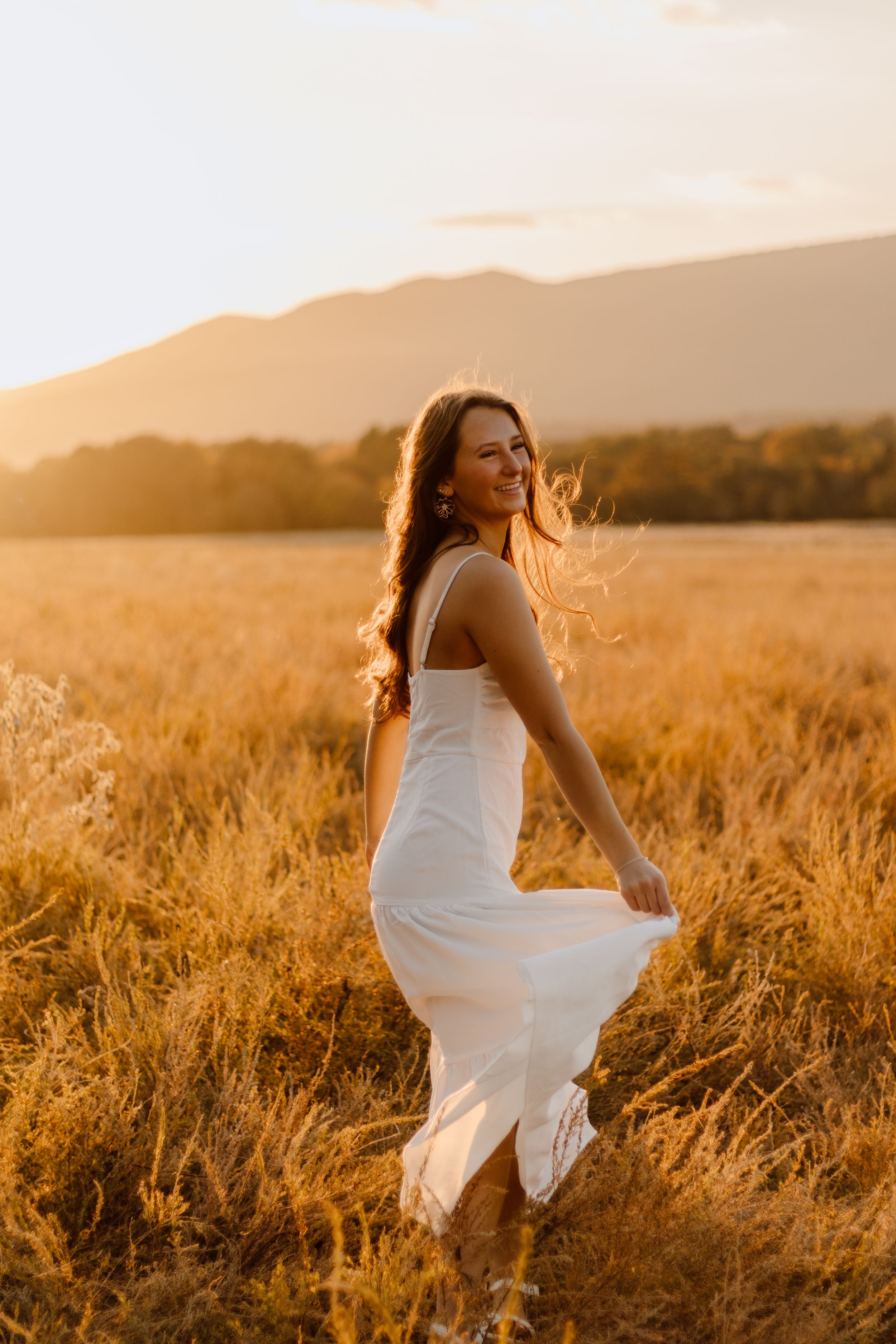 A person in a flowing white dress twirls in a sunlit golden wheat field at sunset.