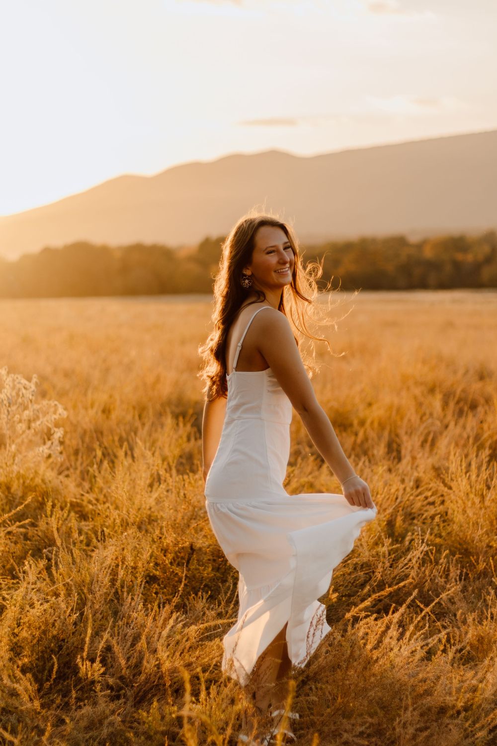 A person in a flowing white dress twirls in a sunlit golden wheat field at sunset.