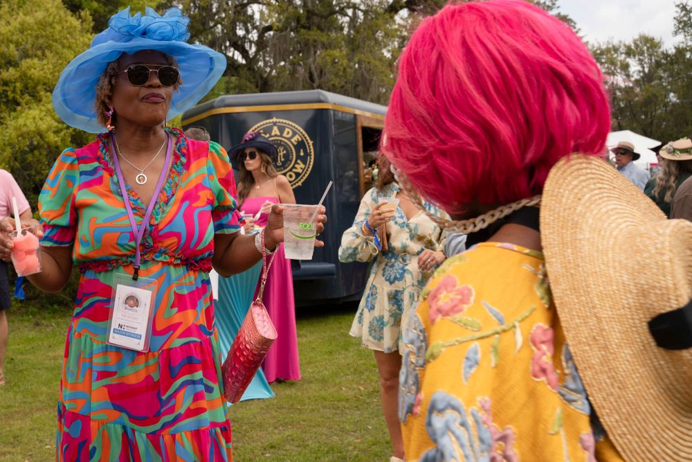 Guests in colorful dresses and sun hats socializing at garden party.