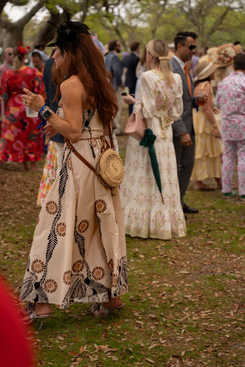 Woman in patterned sundress with wicker purse at outdoor garden party.