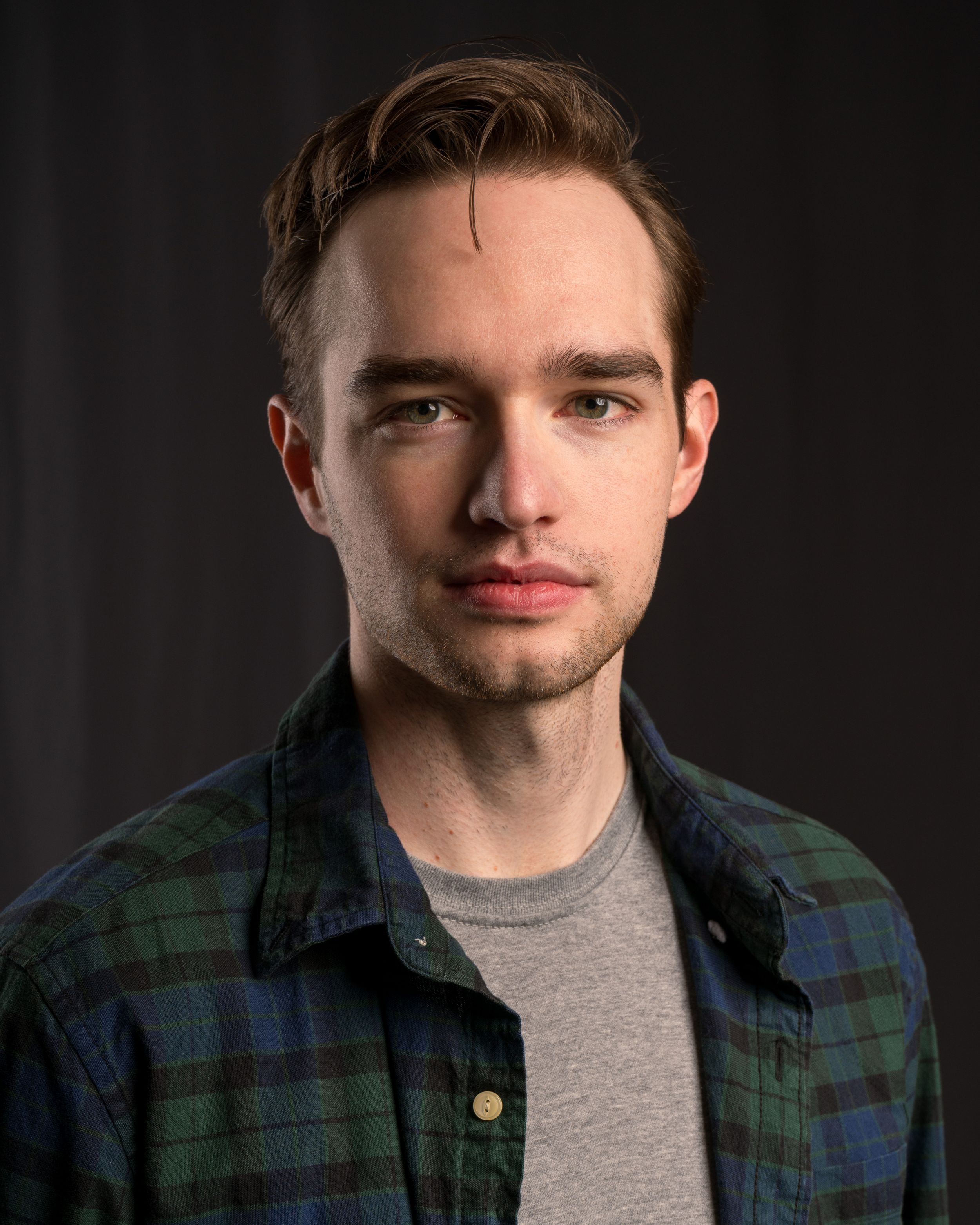 Studio portrait of a person wearing a plaid flannel shirt over a gray t-shirt.