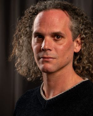 Studio portrait of a person with long curly hair wearing a black sweater.