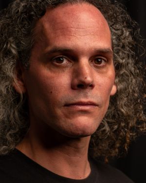 Close-up portrait of a person with curly dark hair against a black background.