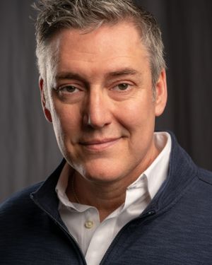 Professional headshot of a person in a navy sweater and white collar shirt.