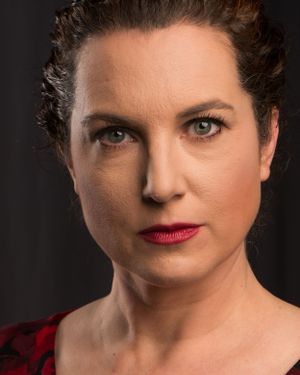 Professional headshot portrait with red lips and dark background in dramatic lighting.