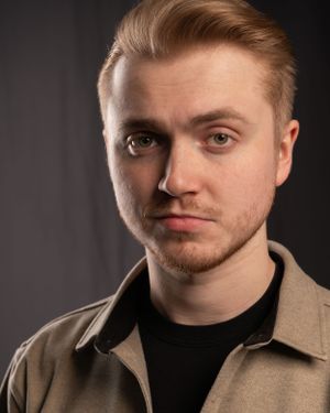 Studio portrait of young person in black shirt and tan jacket.