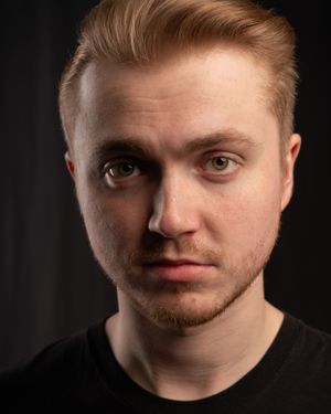 Portrait of young blonde person in dark shirt against black background.