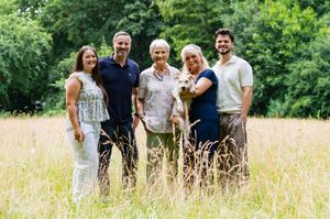 Happy family of five poses together in golden wildflower meadow surrounded by lush green trees.