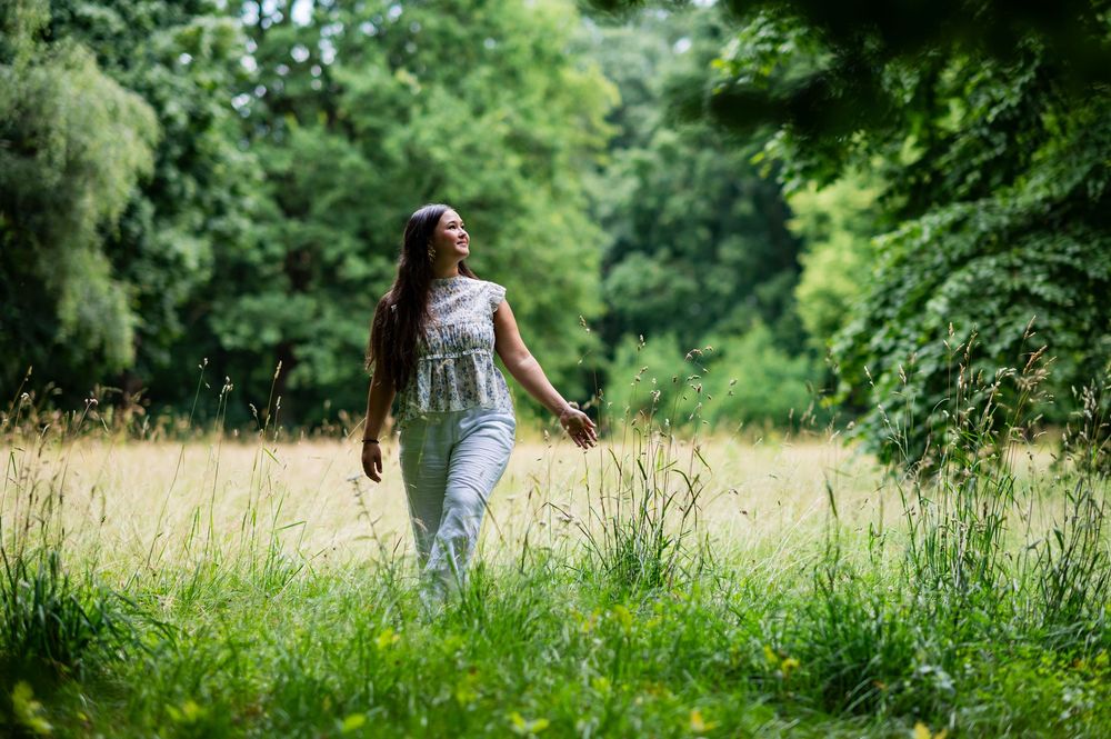 Young woman with long hair walks peacefully through lush green forest path on a bright summer day.
