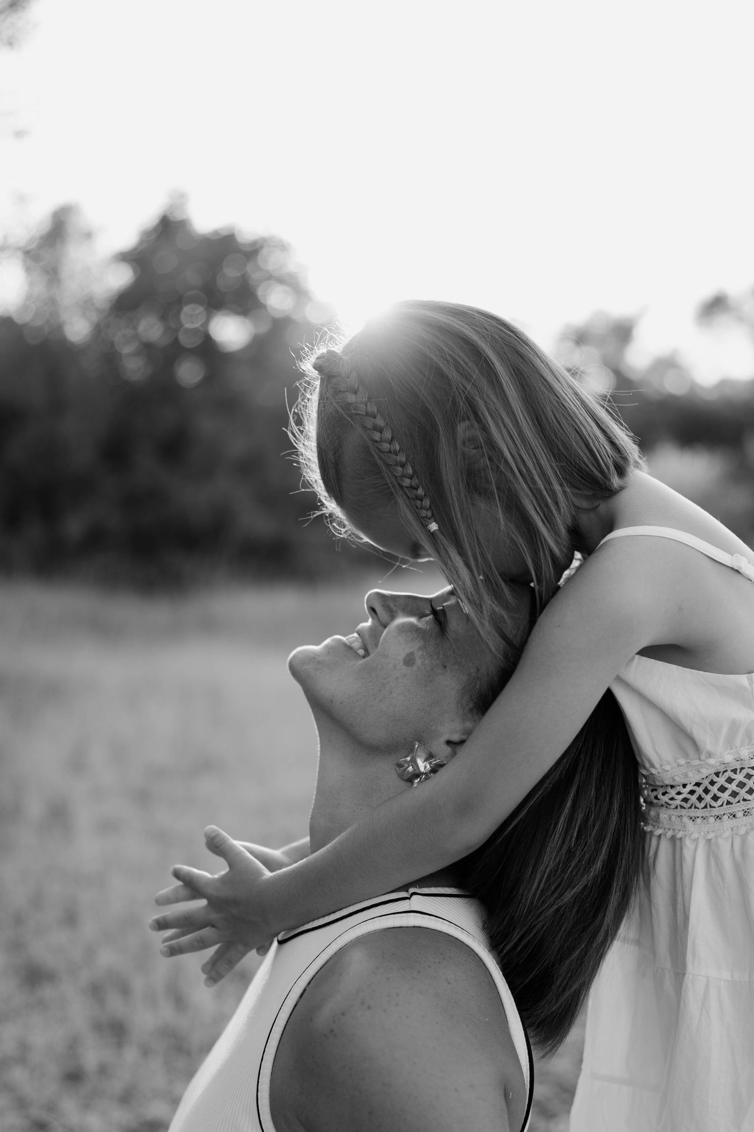 A black and white photo showing an intimate embrace in a sun-drenched field during golden hour.