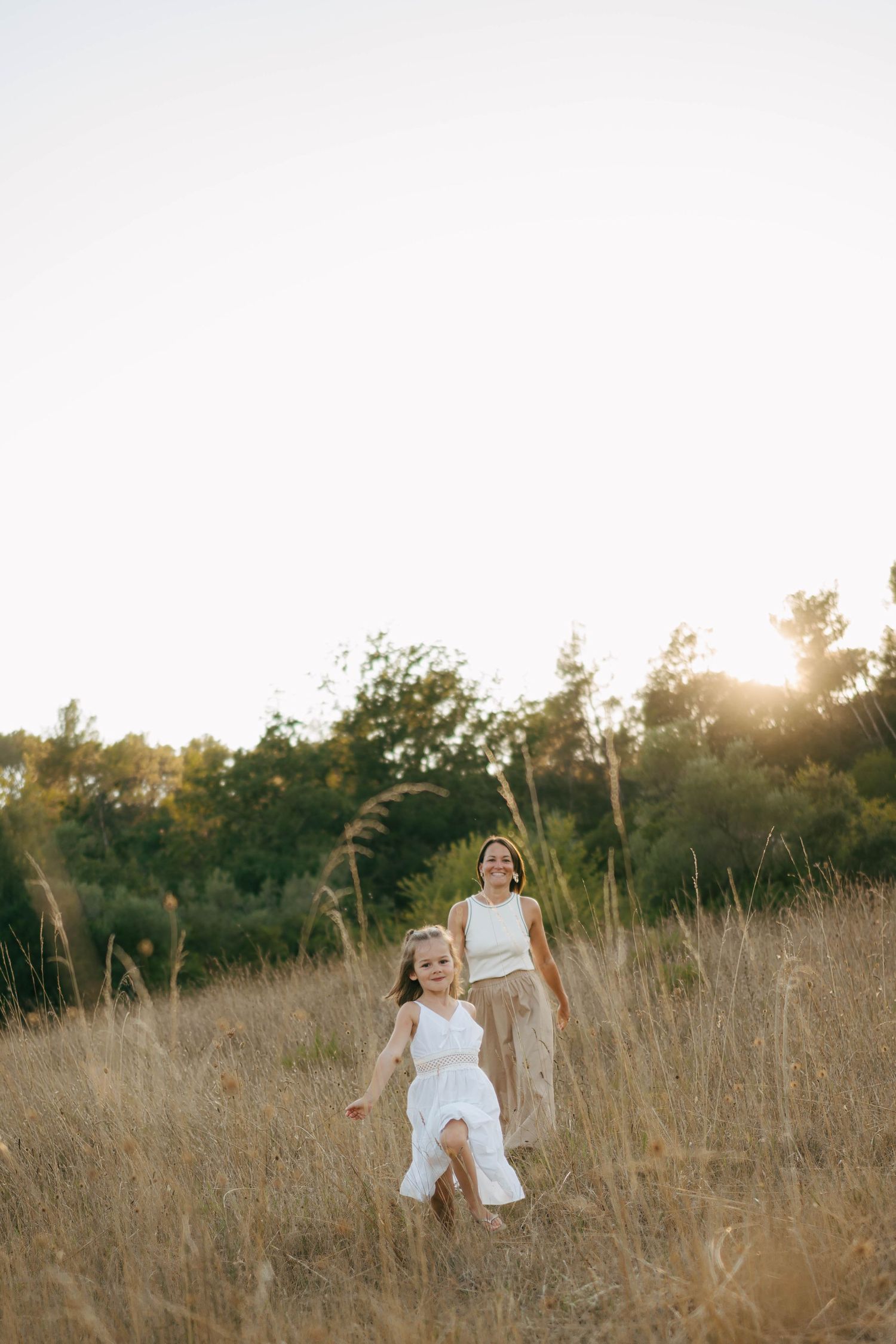 Une femme en robe blanche tourne joyeusement dans un champ doré au coucher du soleil, créant un mouvement éthéré dans l'herbe haute. Photo