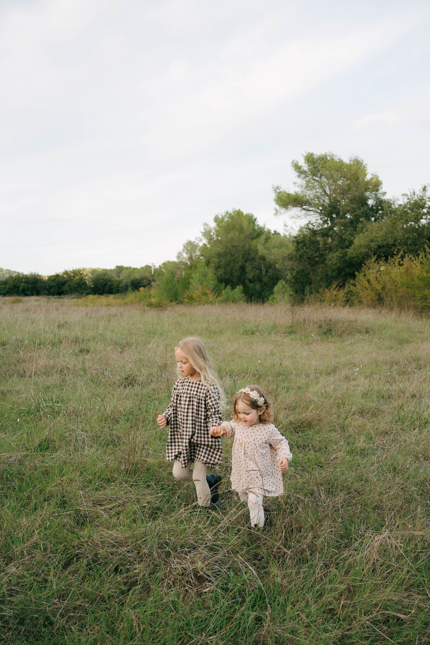 Two children walk together through a grassy meadow on an autumn afternoon.