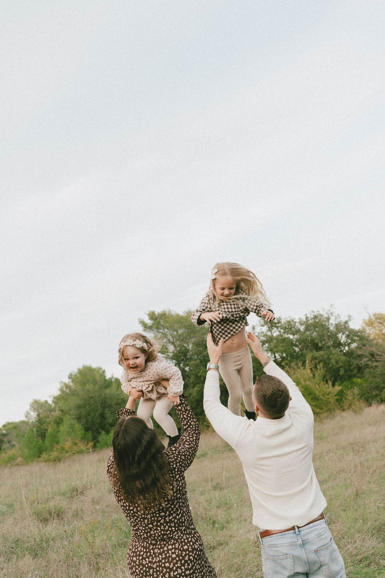 A couple in casual attire plays and dances together in a grassy field during a sunny day.