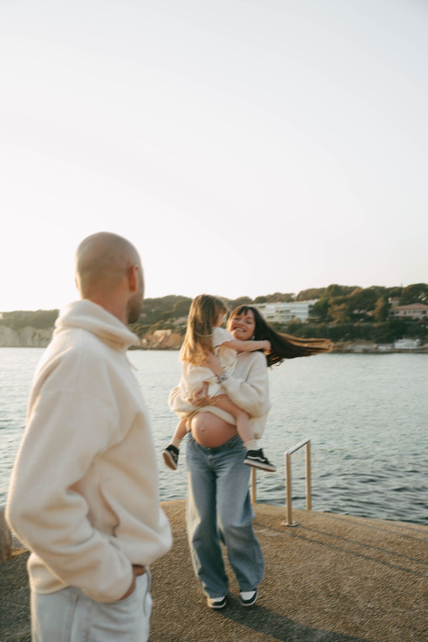 Three connected photos show people embracing on a waterfront pier at sunset with a coastal landscape in the background.