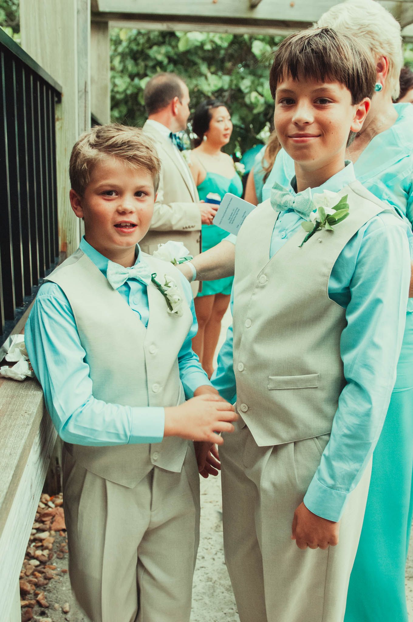 Two young attendants in matching turquoise shirts and tan vests smile at the camera.