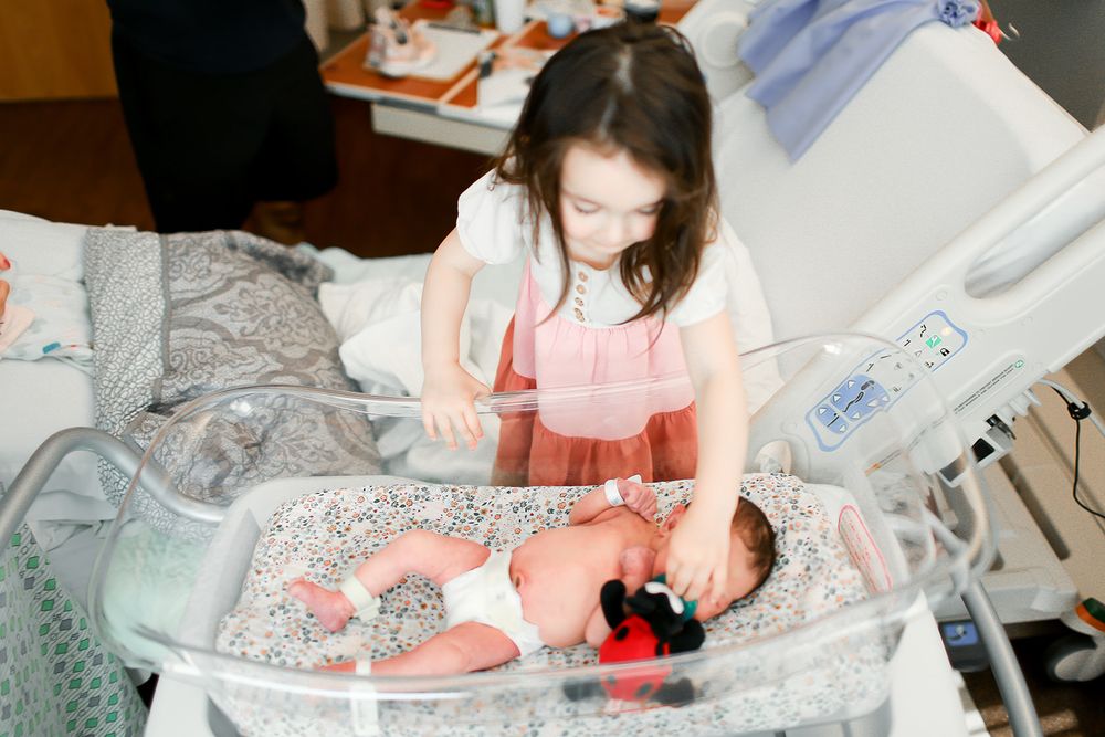 Big sister giving newborn sister a Paci in hospital bed