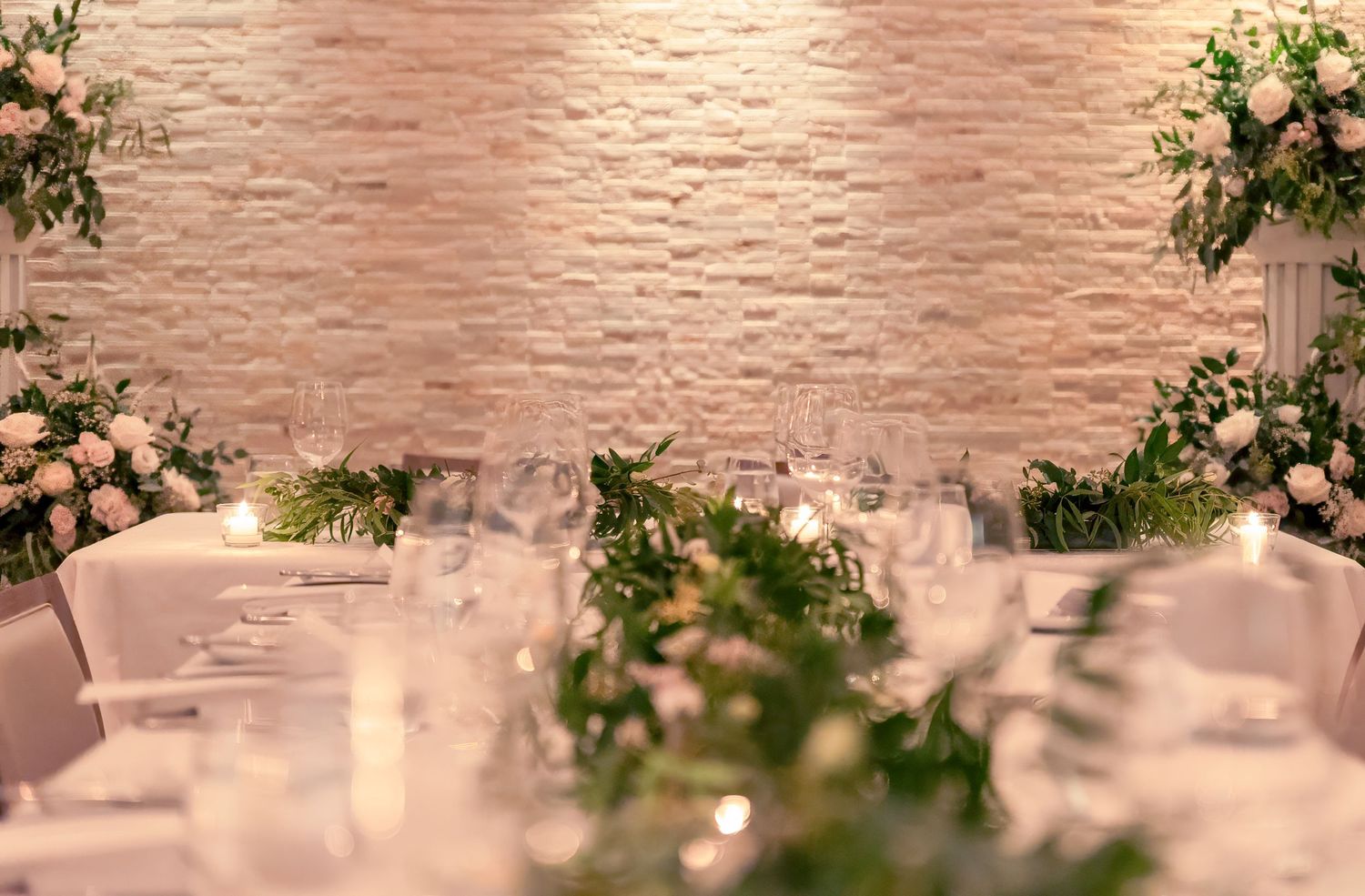 An elegant wedding reception setting with ghost chairs and peach floral arrangements against a textured pink wall.