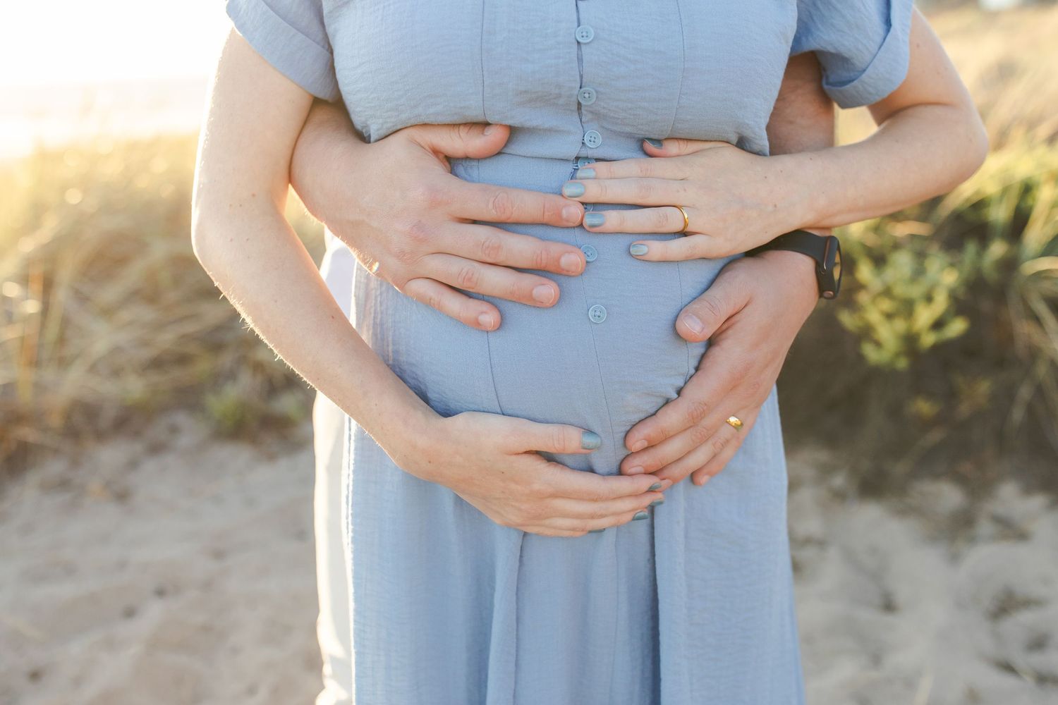 A series of close-up photos showing hands cradling a pregnant belly in a light blue dress outdoors at sunset.