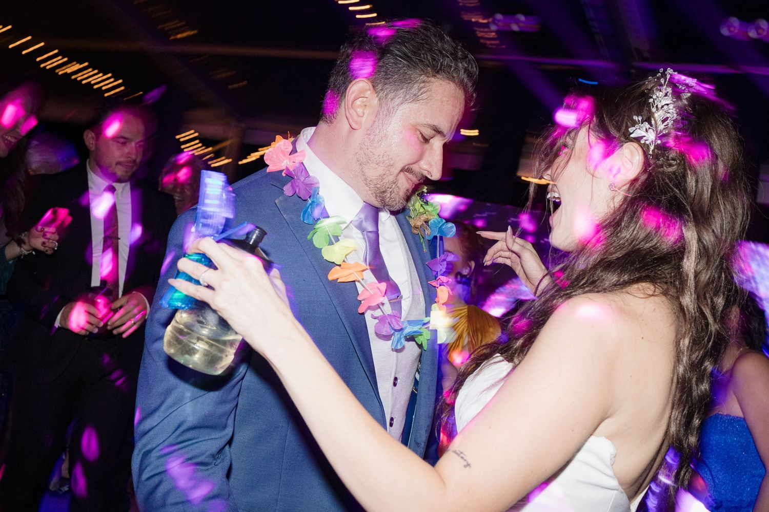 Wedding reception dance party with colorful purple lighting and energetic crowd.