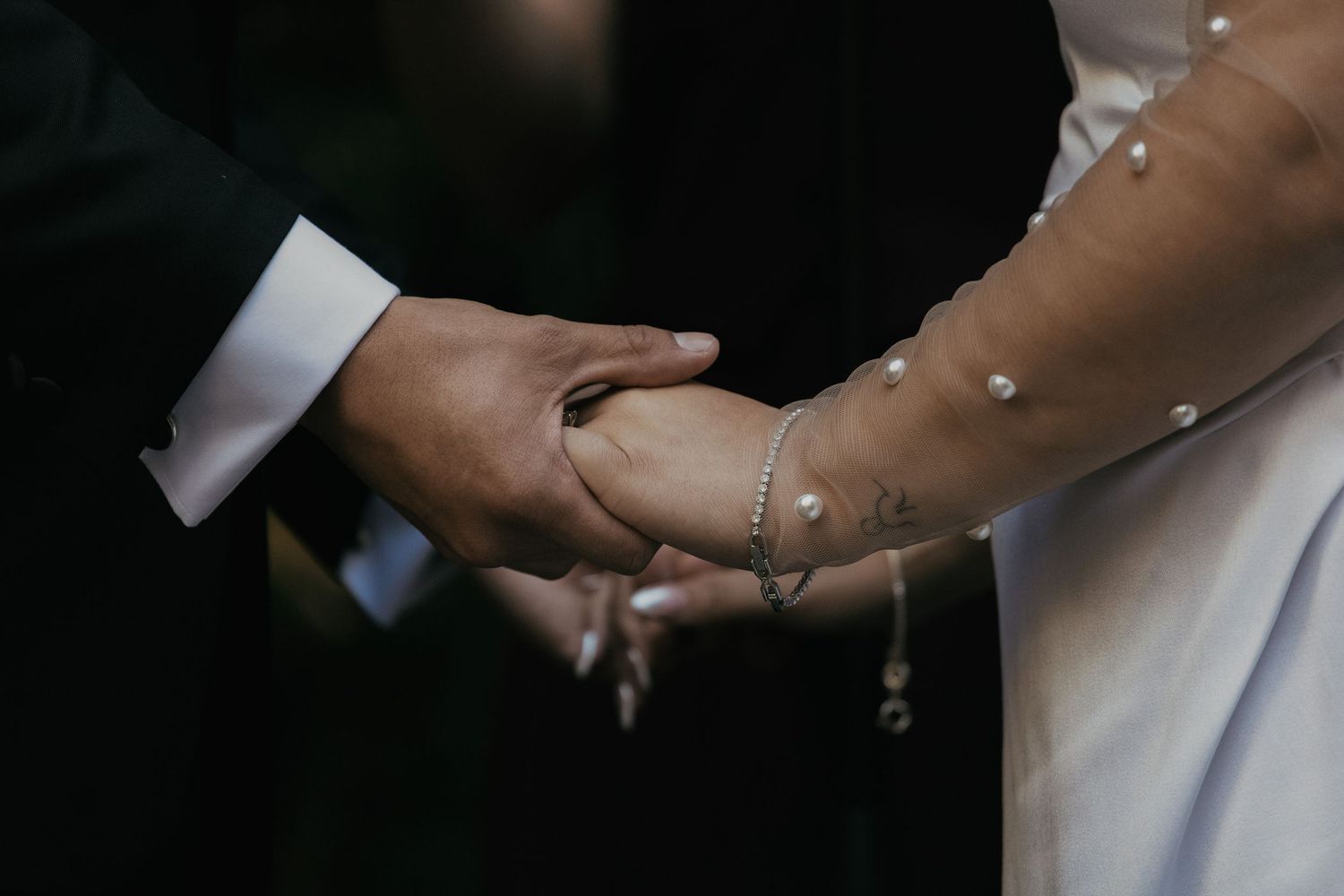 A bride and groom holding hands during their wedding ceremony while a celebrant stands nearby.