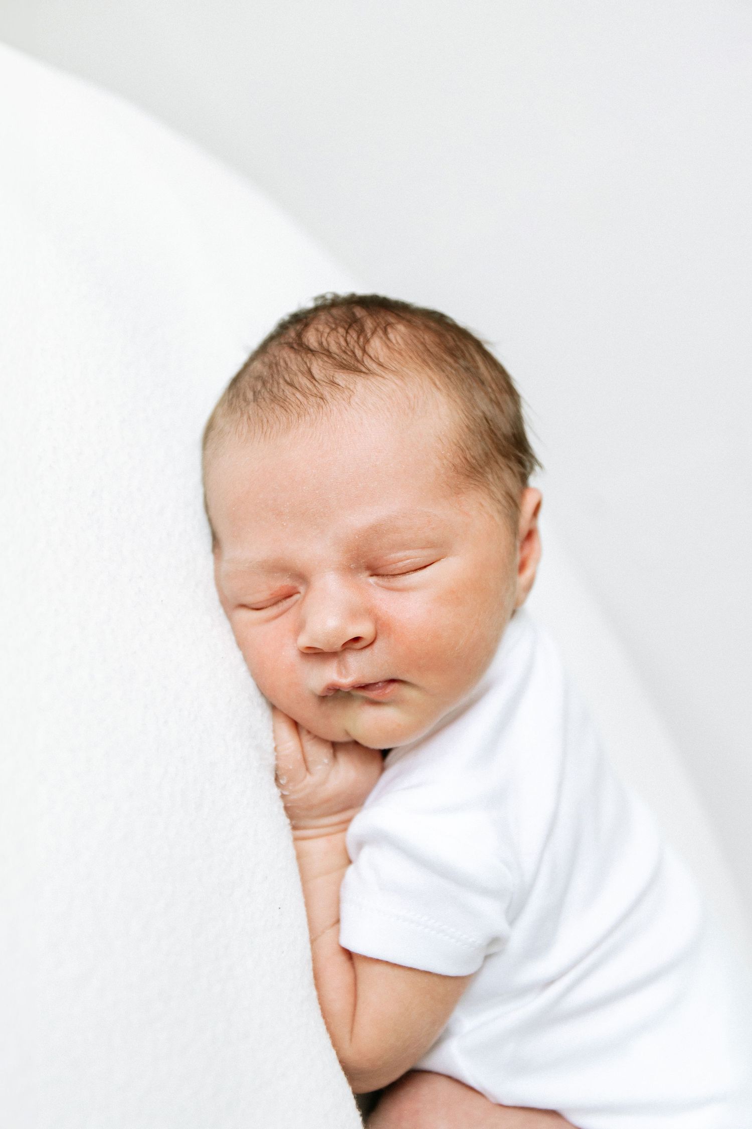 Peaceful sleeping newborn baby in white clothing against a light background, during newborn shoot in Nottingham