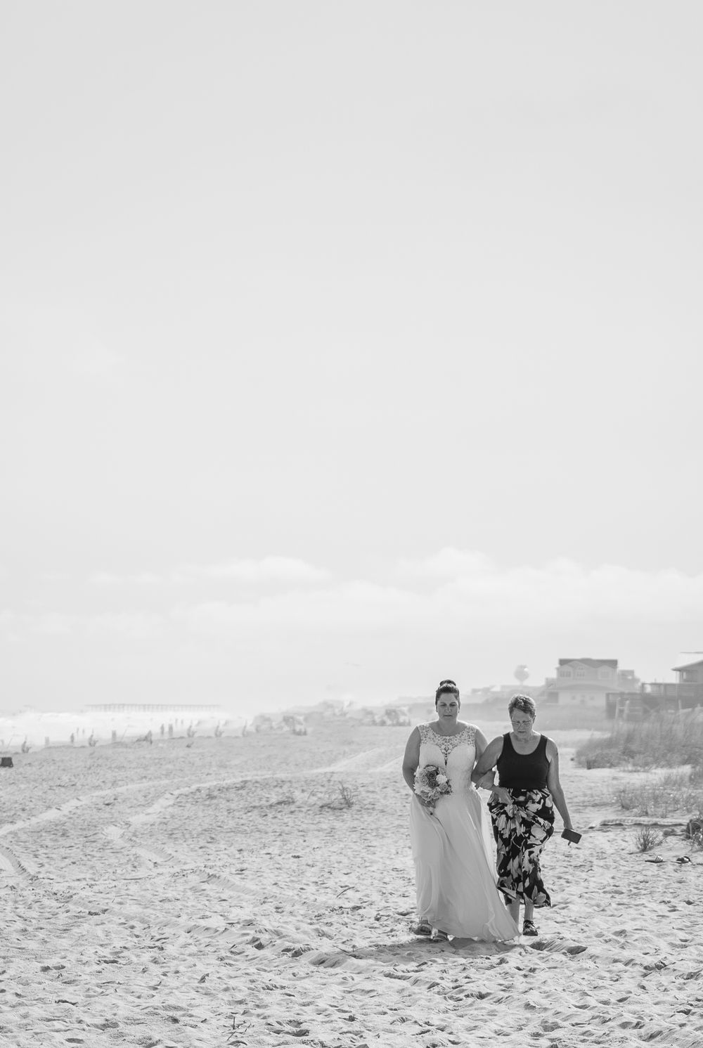 A bride being walked down the aisle on a misty beach with grasses in the foreground during a wedding ceremony.